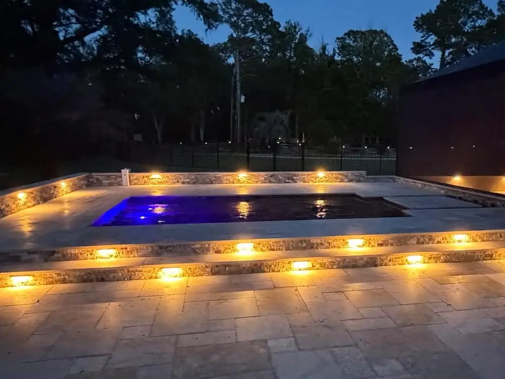 inground pool with deck lights at night